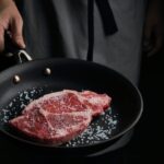 person cooking meat on black pan
